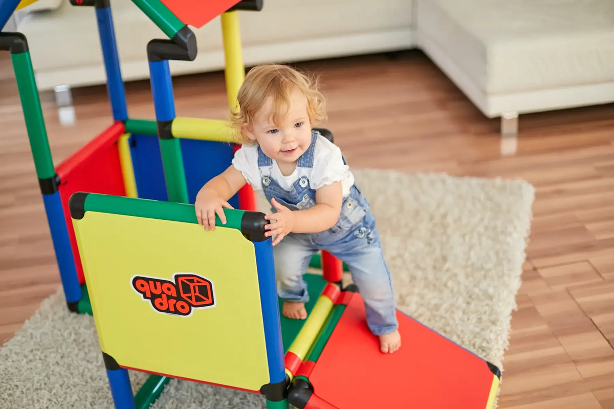 Toddler standing inside a colourful QUADRO play structure and holding a yellow panel