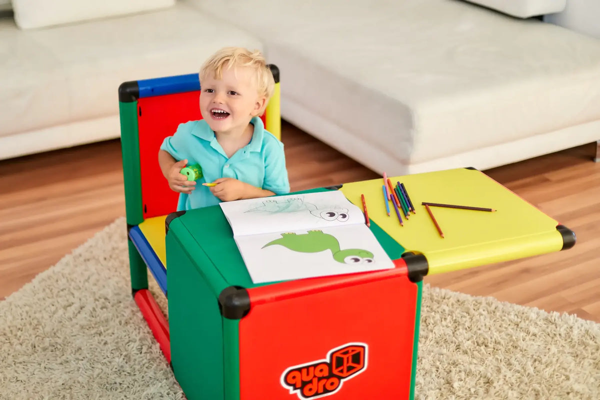Smiling child drawing at a compact red and yellow QUADRO play table