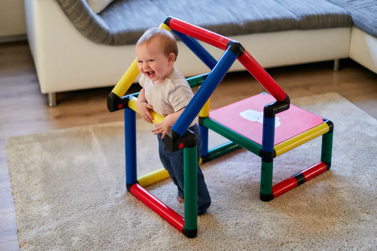 Toddler holding a small QUADRO play table beside a triangular climbing frame