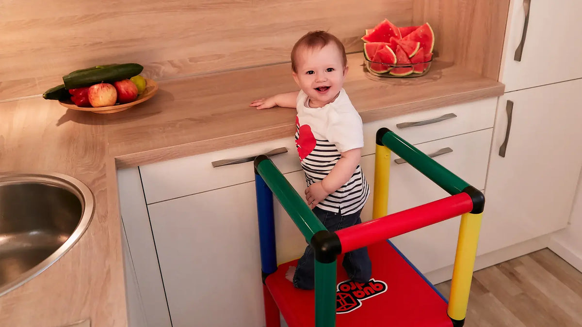 Toddler standing safely in a colourful QUADRO learning tower at a kitchen counter