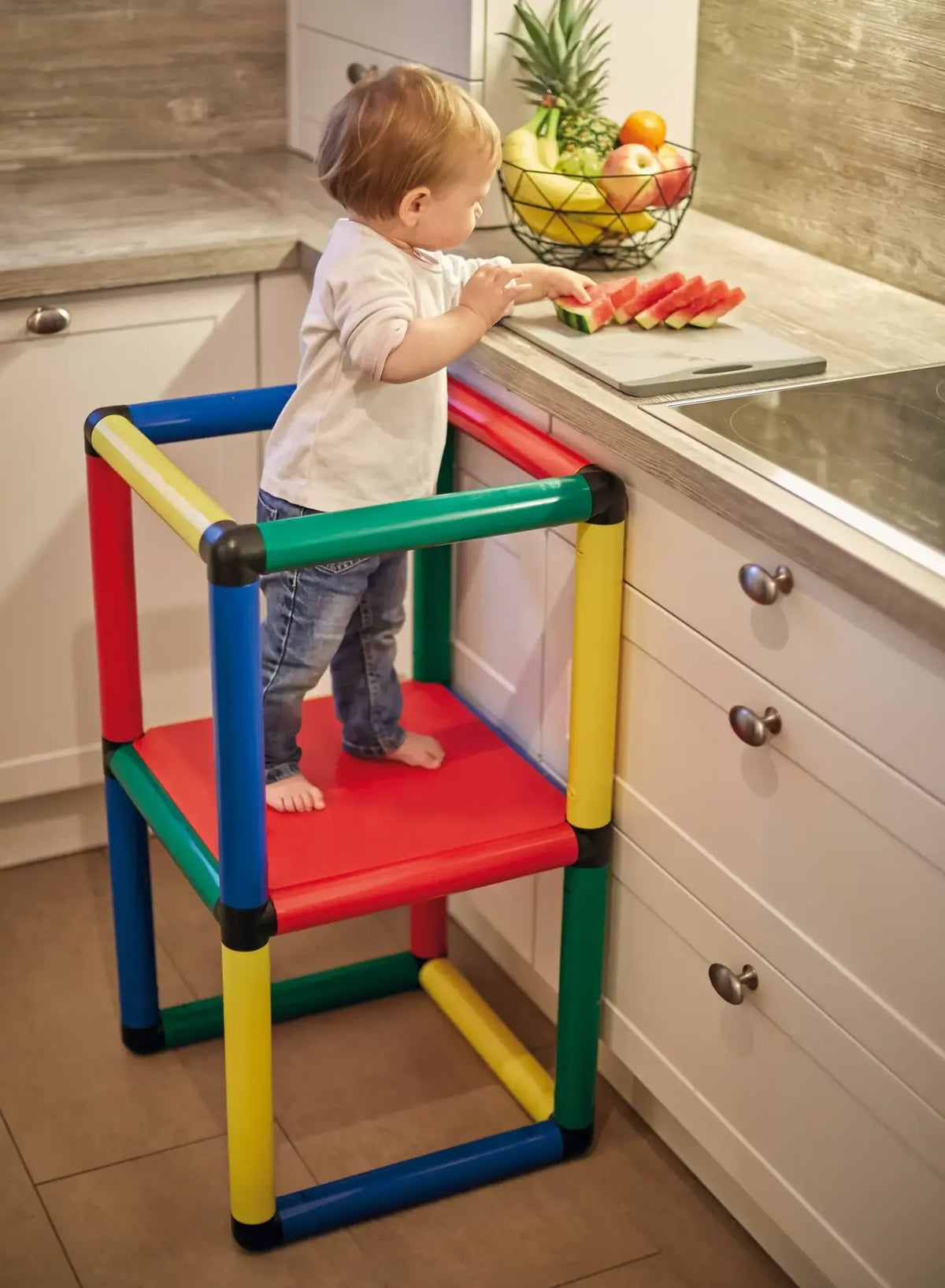 Child using a colourful QUADRO learning tower at a kitchen worktop