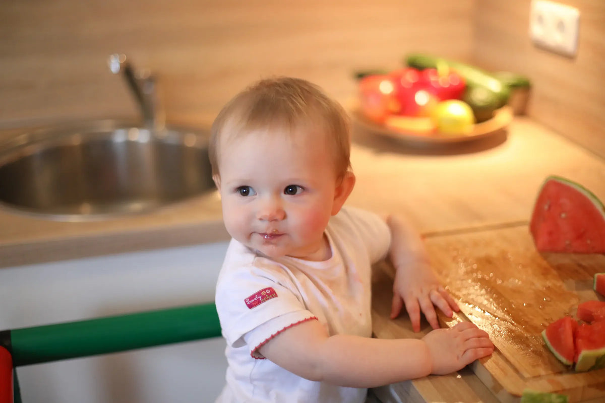 Toddler leaning on the green rail of a QUADRO learning tower in a kitchen
