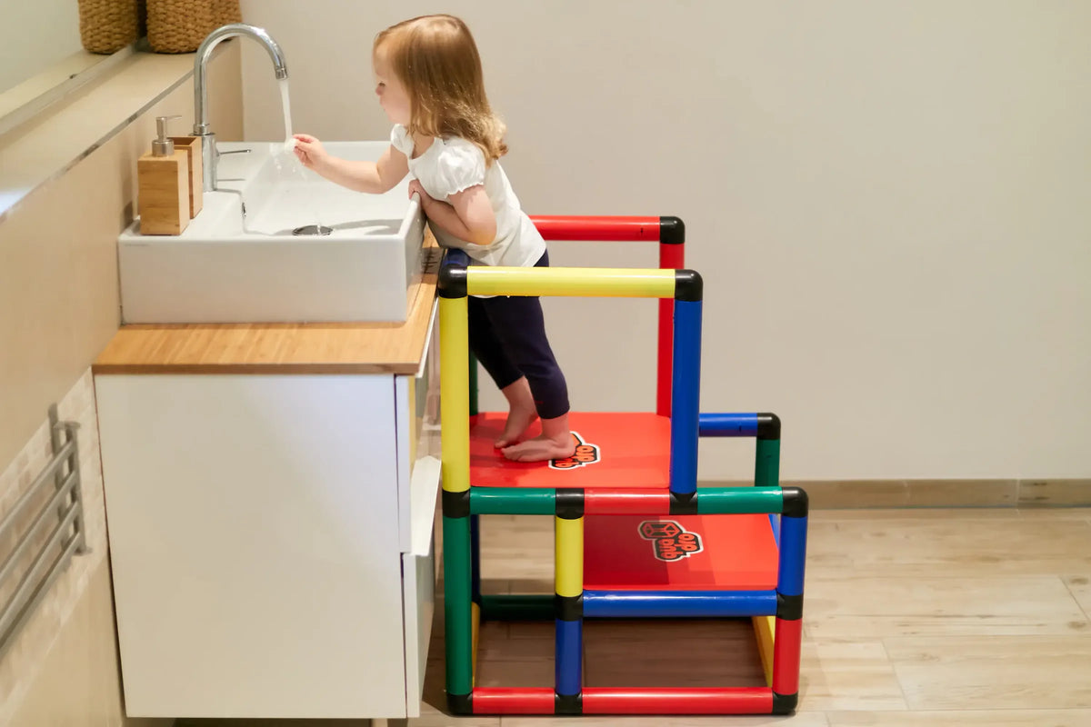 Child standing on a red QUADRO learning tower platform beside a sink
