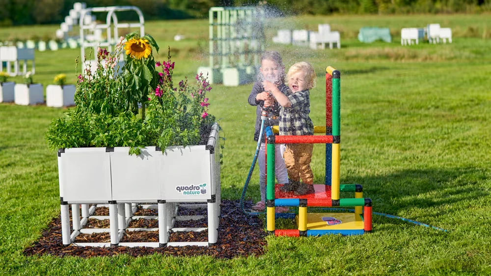 Two children gardening beside a QUADRO learning tower in a community garden