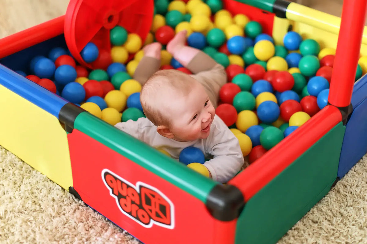 Baby lying in a colourful ball pool built from QUADRO Evolution panels