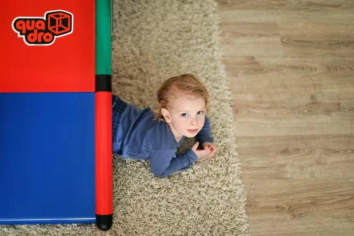 Toddler peeking out beside a red and blue QUADRO Evolution play cube
