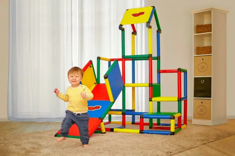 Toddler standing beside a tall indoor QUADRO climbing tower with panels